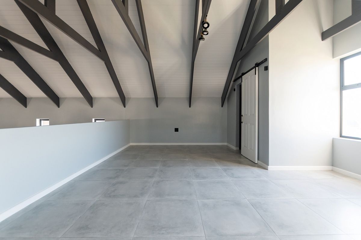 Spacious open-plan living area featuring a high vaulted ceiling with exposed timber rafters, modern tiled flooring, and a stylish sliding barn door.
