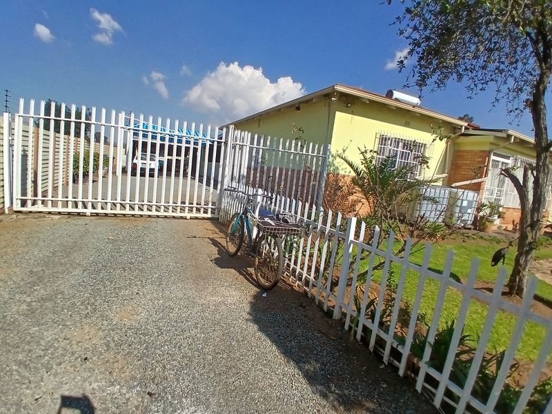 Front exterior view of the property featuring a gravel driveway, secure metal perimeter fencing, and a solar water heater installed on the roof.