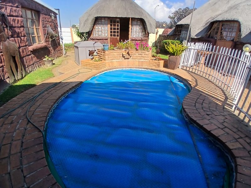 Outdoor pool area featuring a swimming pool with a cover, surrounded by brick paving, planter boxes, and traditional thatched-roof structures.