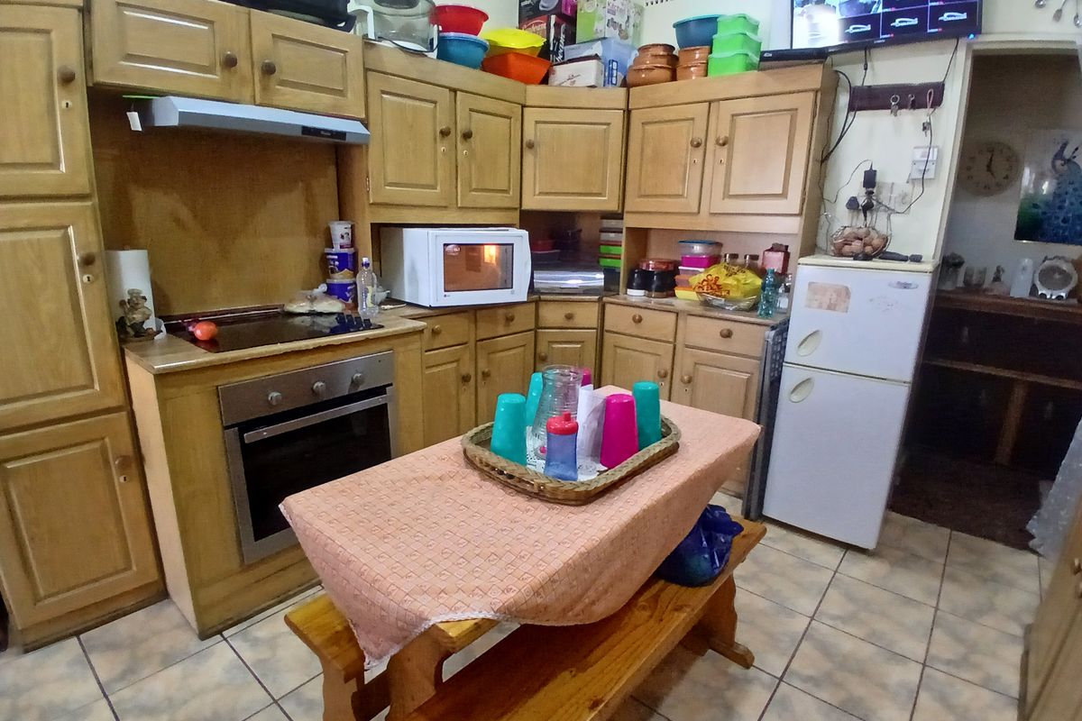 A functional kitchen featuring traditional wooden cabinetry, integrated oven and hob, and tiled flooring, offering a classic layout with ample storage space.