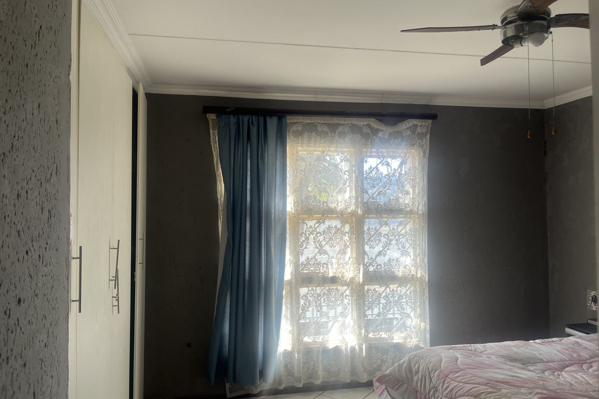 Bedroom featuring built-in cupboards, tiled flooring, and a ceiling fan, with natural light entering through a window.