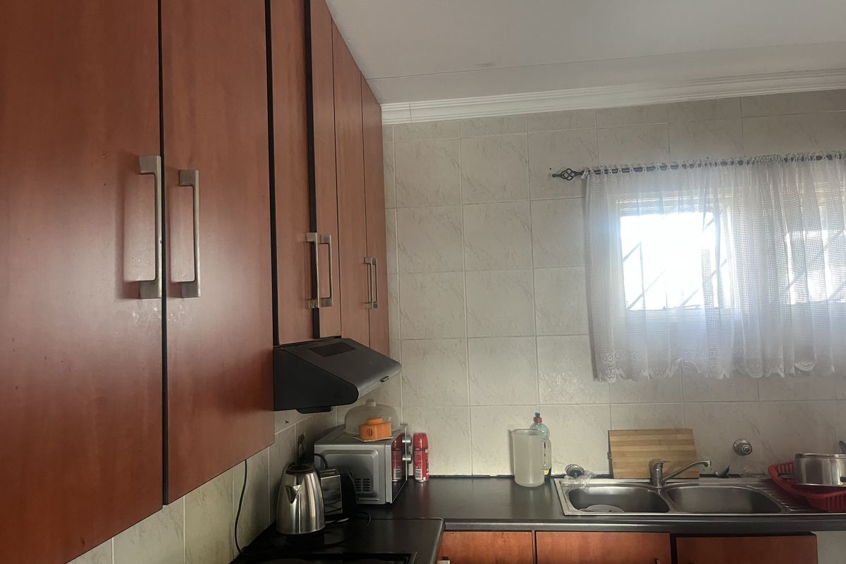 A functional kitchen featuring wood-finish cabinetry, a tiled backsplash, a stainless steel double sink, and an integrated extractor fan.