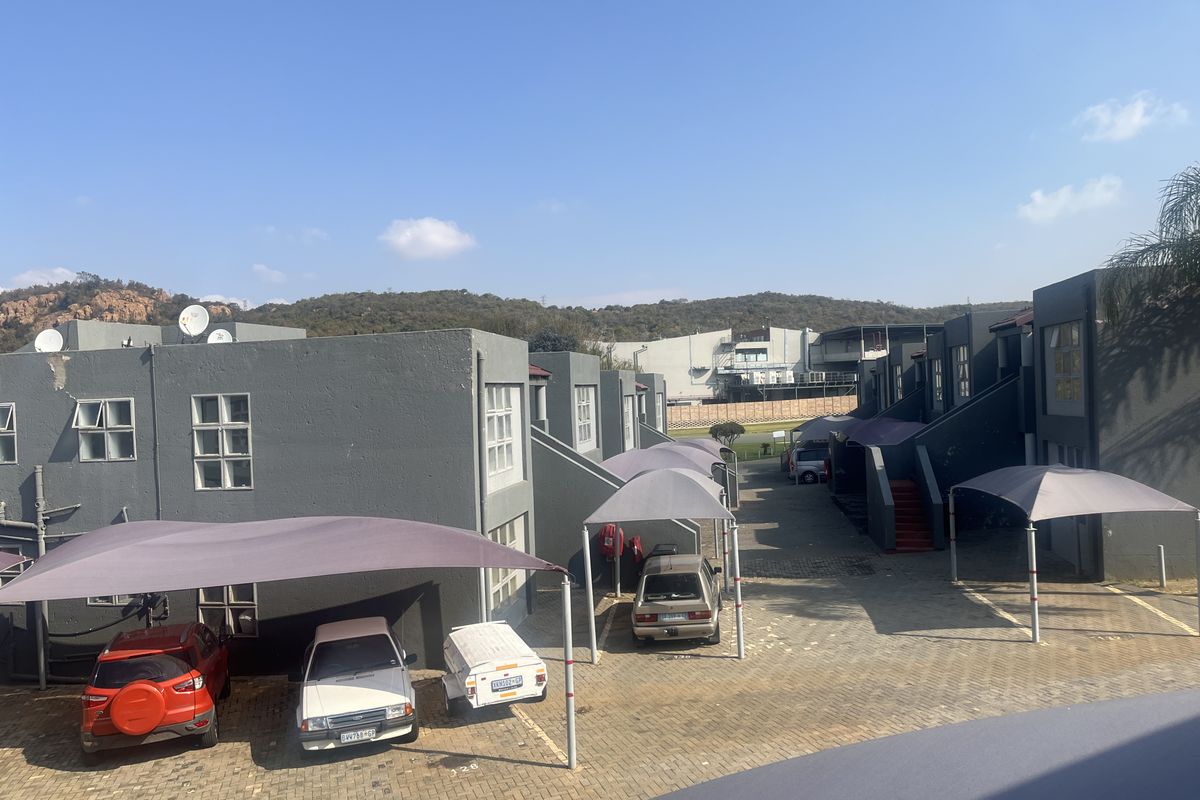 Exterior view of an apartment complex featuring paved parking areas with shade cloth carports and multi-level residential units.