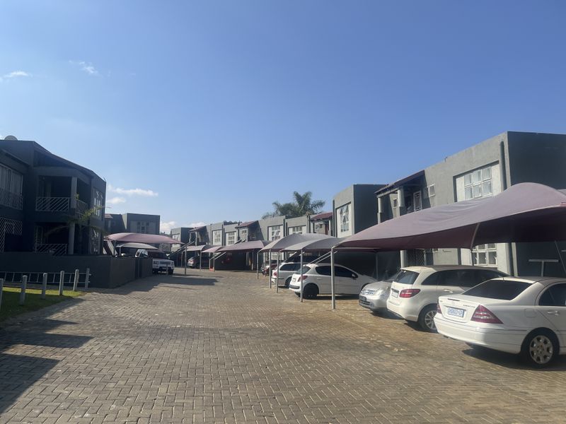 Exterior view of a residential apartment complex featuring paved parking areas and covered carports for residents.