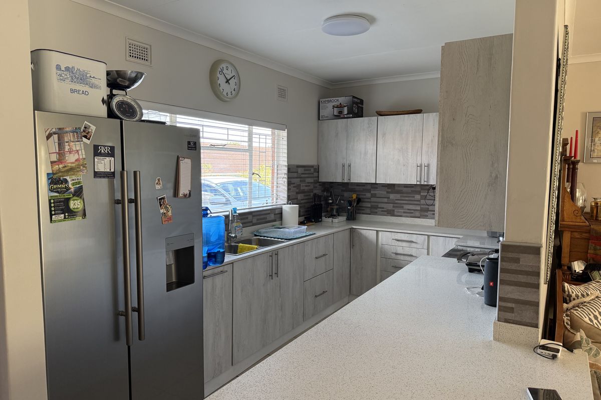 A functional kitchen featuring light wood-grain cabinetry, stone-look countertops, a tiled backsplash, and a breakfast bar overlooking the living area.