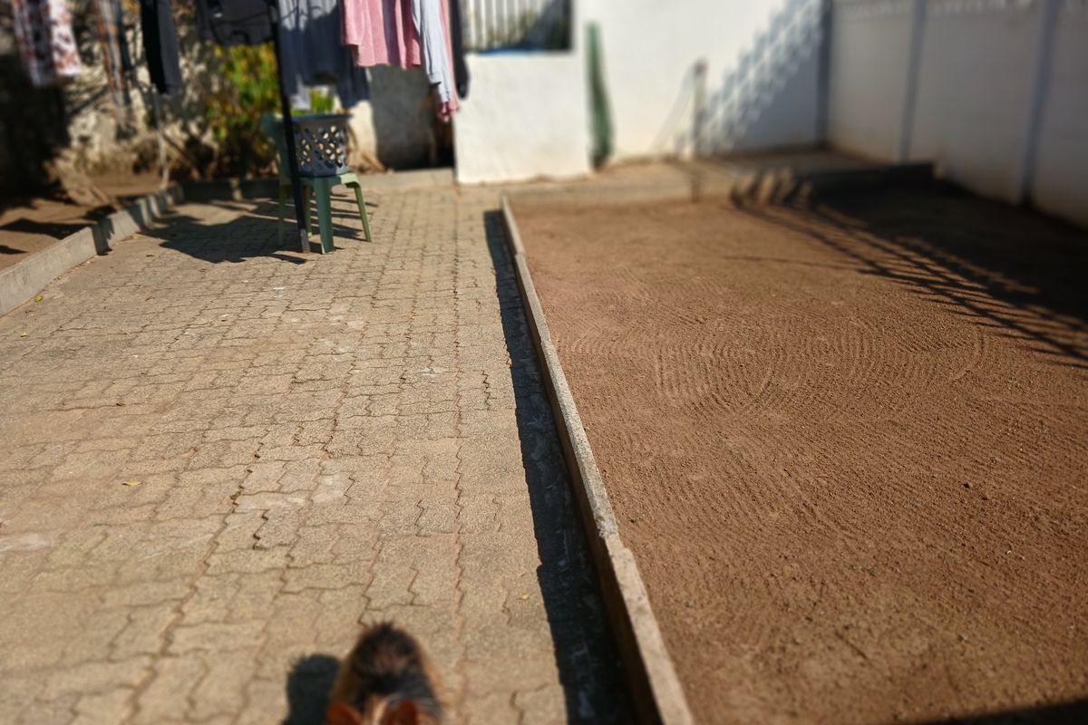 Rear outdoor area featuring paved walkway and a leveled sand section enclosed by a boundary wall.