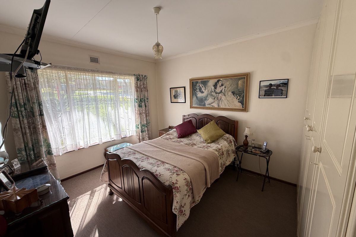 A standard bedroom featuring built-in wardrobes, carpeted flooring, and a large window providing natural light.