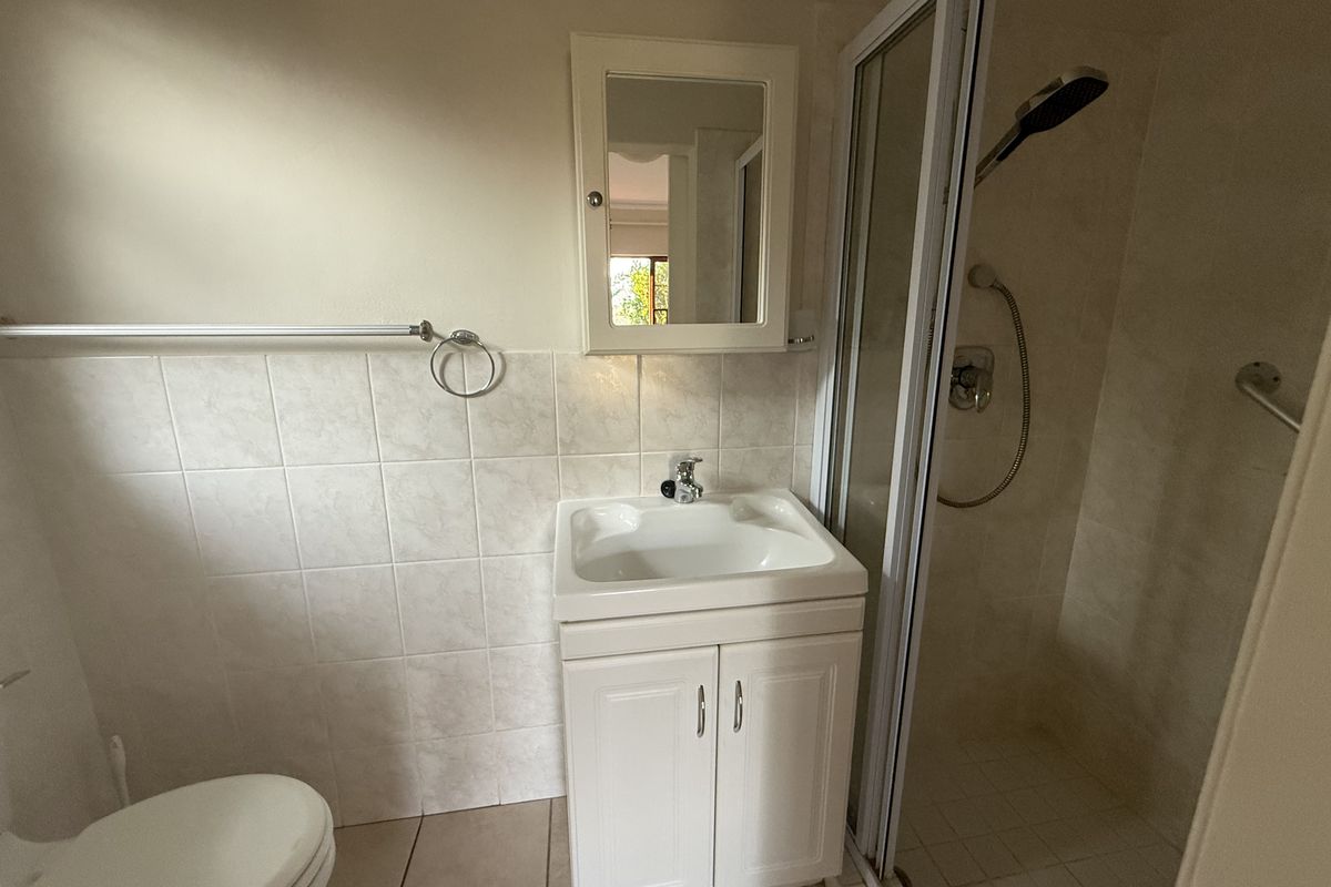 A functional bathroom featuring a vanity cabinet with basin, a shower enclosure, and a wall-mounted medicine cabinet with neutral wall tiling.