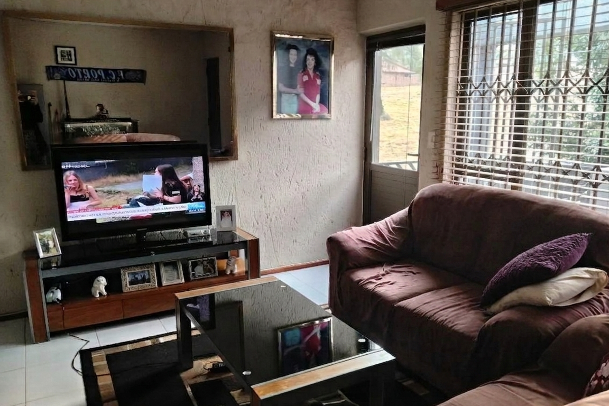 A living room featuring tiled flooring, a large wall mirror, and a security gate leading to an outdoor area with venetian blinds.