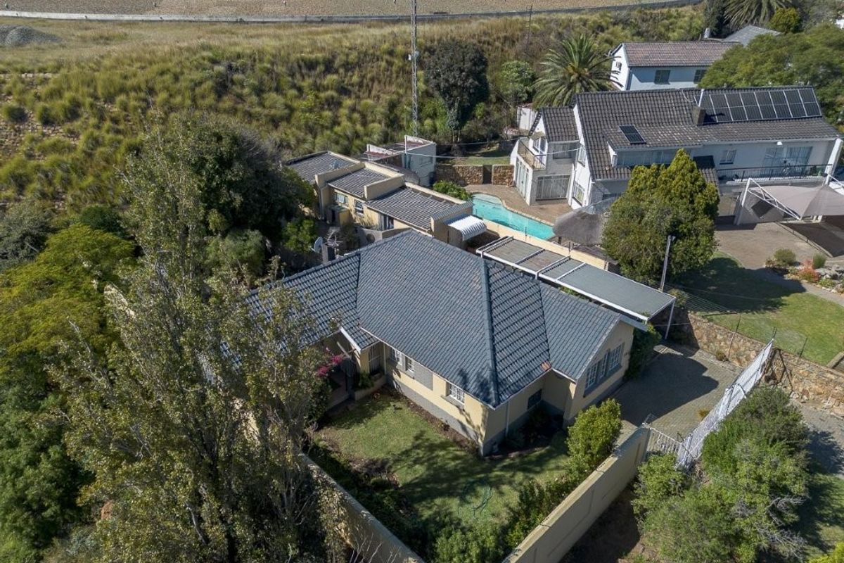 Aerial view of a residential property featuring a tiled roof house, swimming pool, paved driveway, and perimeter walling in a suburban setting.