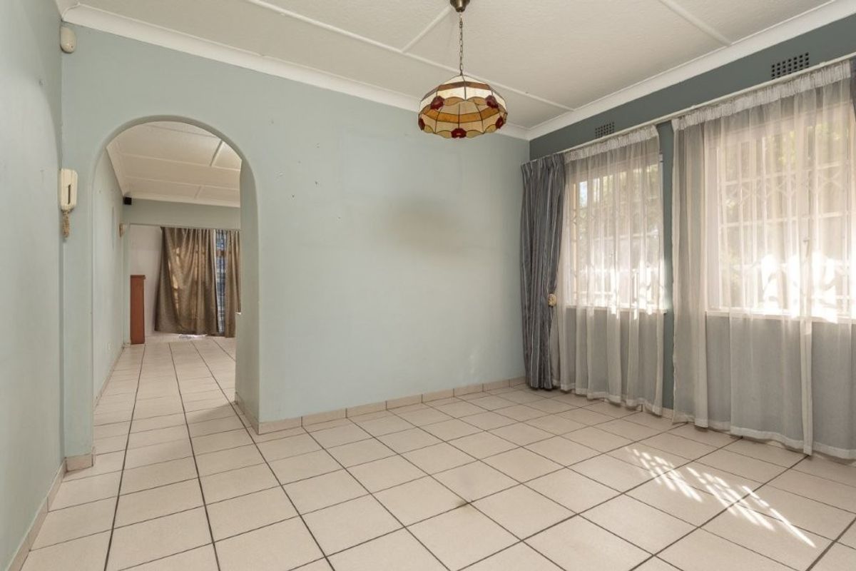 An empty living room featuring tiled flooring, an arched entryway, and large windows with security bars, offering a blank canvas for interior design.