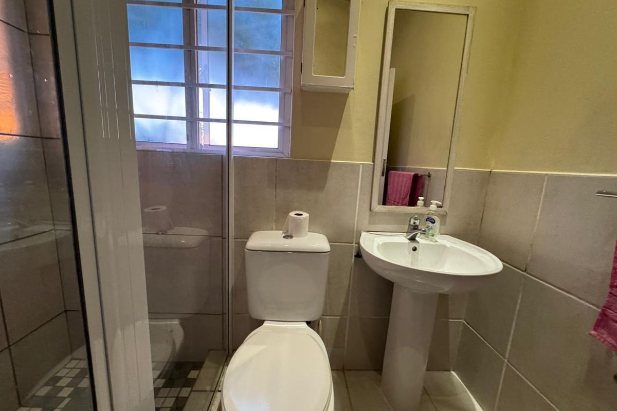 A compact bathroom featuring a pedestal basin, toilet, and a shower enclosure with security bars on the window.