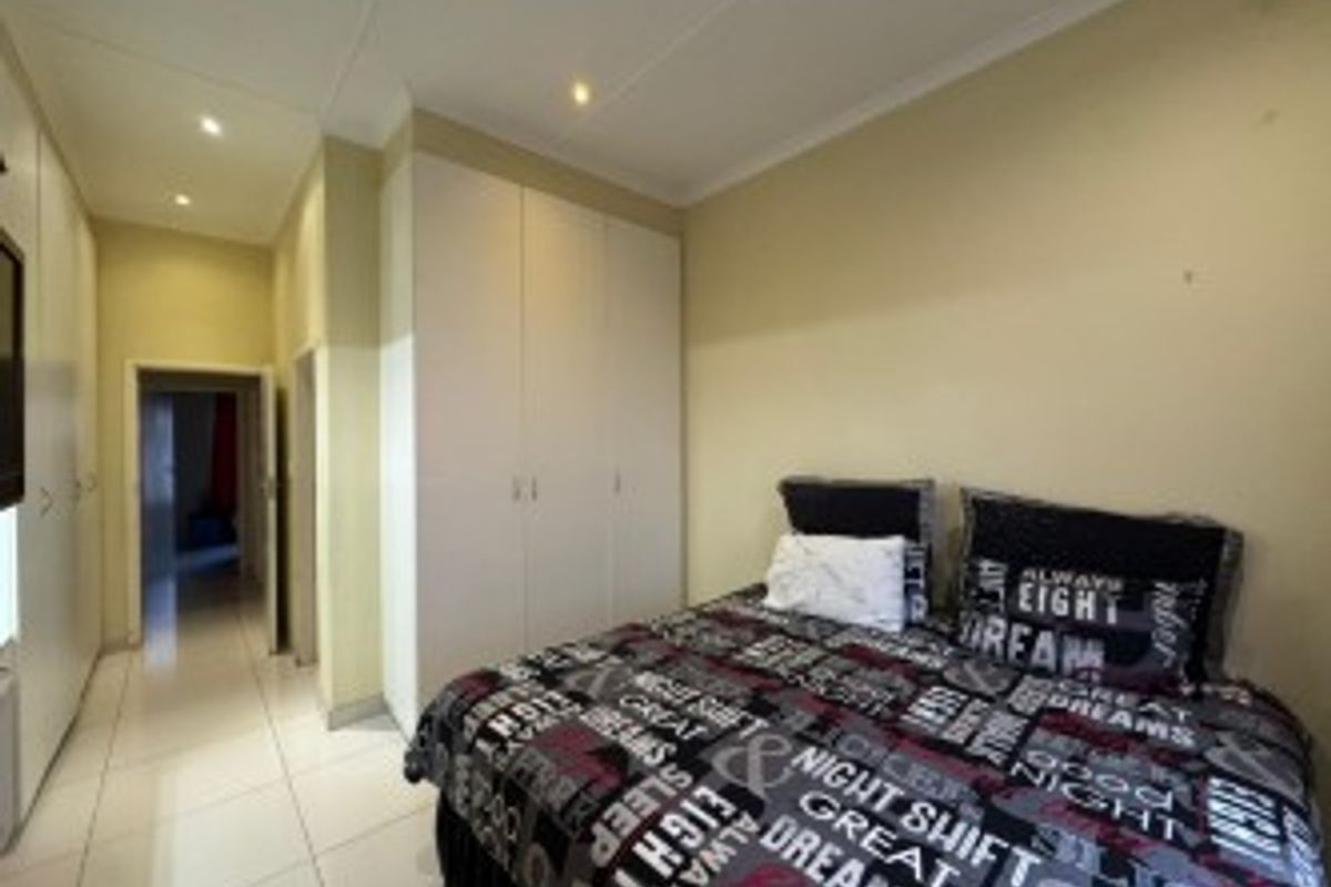 A functional bedroom featuring built-in cupboards, tiled flooring, and recessed downlighting, offering a clean and practical living space.