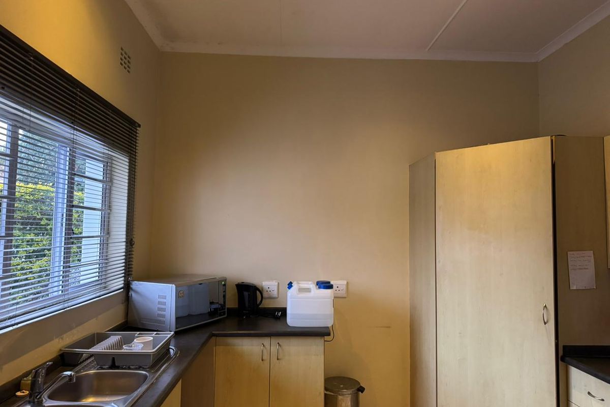A functional kitchen area featuring laminate countertops, double bowl stainless steel sink, and built-in veneer cabinetry with natural light from a window.