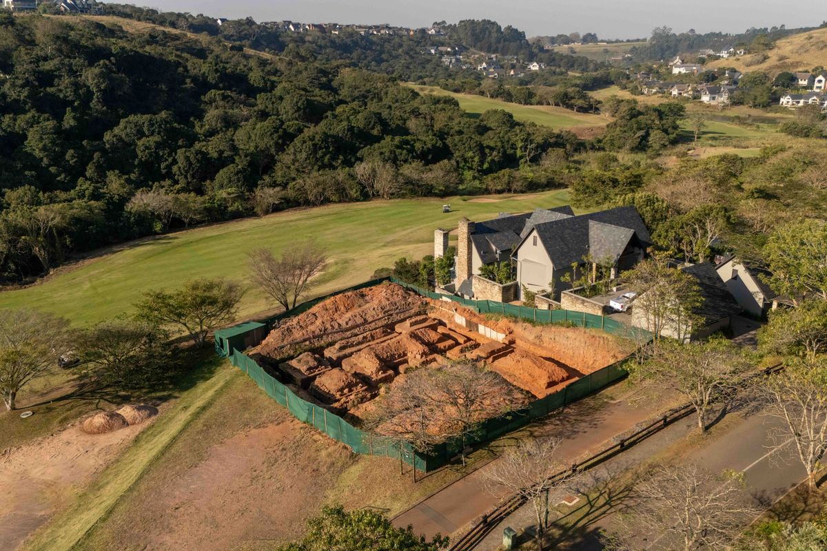 Aerial view of a residential property featuring an adjacent excavated building site, situated within a scenic estate landscape.