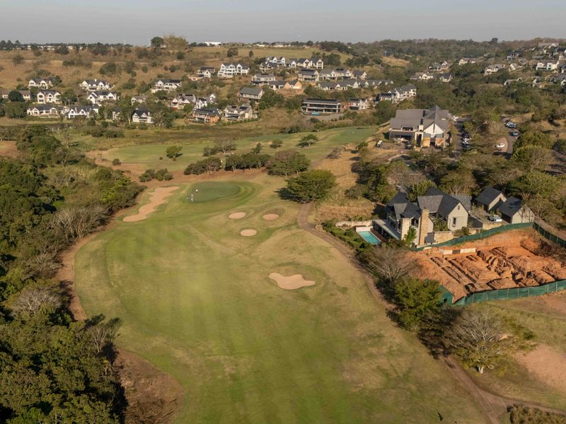 Aerial view of a residential property situated on a golf course, featuring a swimming pool and an adjacent active construction site.