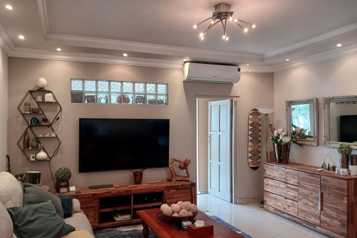 A well-maintained living room featuring recessed ceiling lighting, crown molding, a split-system air conditioner, and decorative glass block windows.