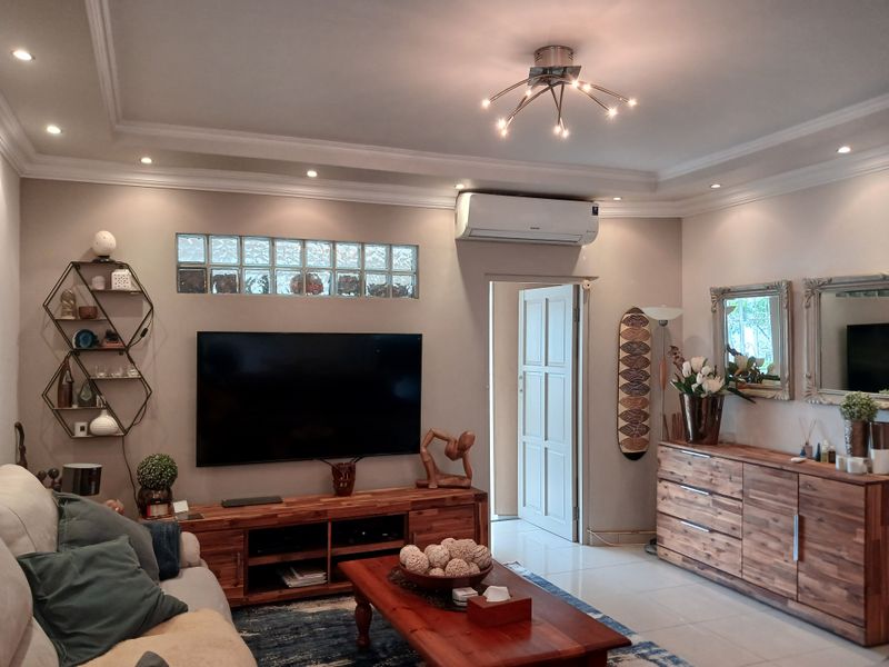 A well-maintained living room featuring recessed ceiling lighting, crown molding, a split-system air conditioner, and decorative glass block windows.