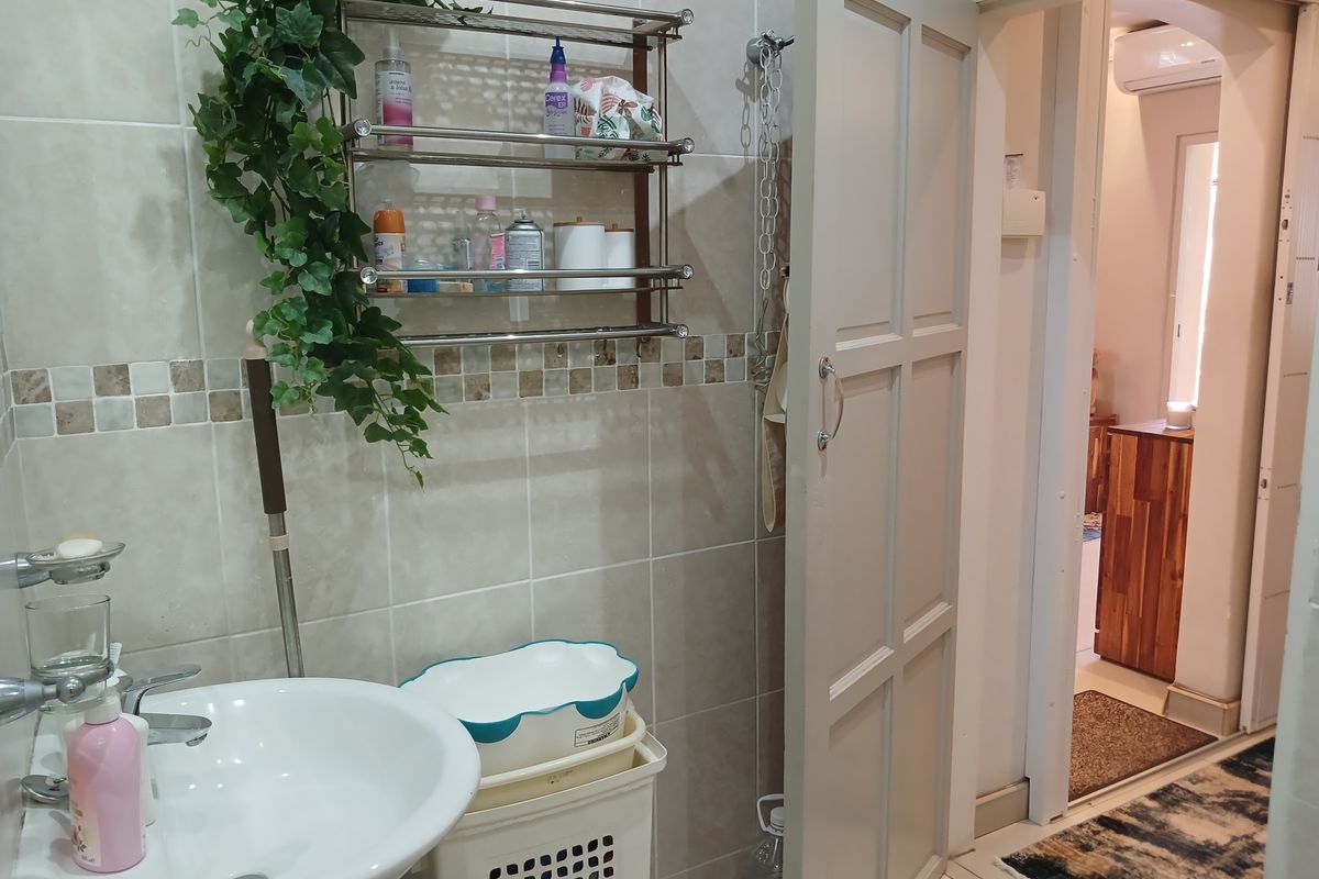 A functional bathroom featuring neutral ceramic wall tiles, a pedestal washbasin with chrome fixtures, and a wall-mounted storage shelf.