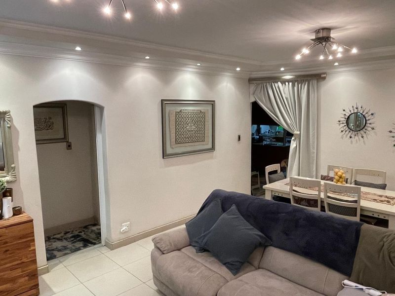 An open-plan living and dining area featuring tiled flooring, recessed downlighting, and an arched entryway leading to adjacent spaces.