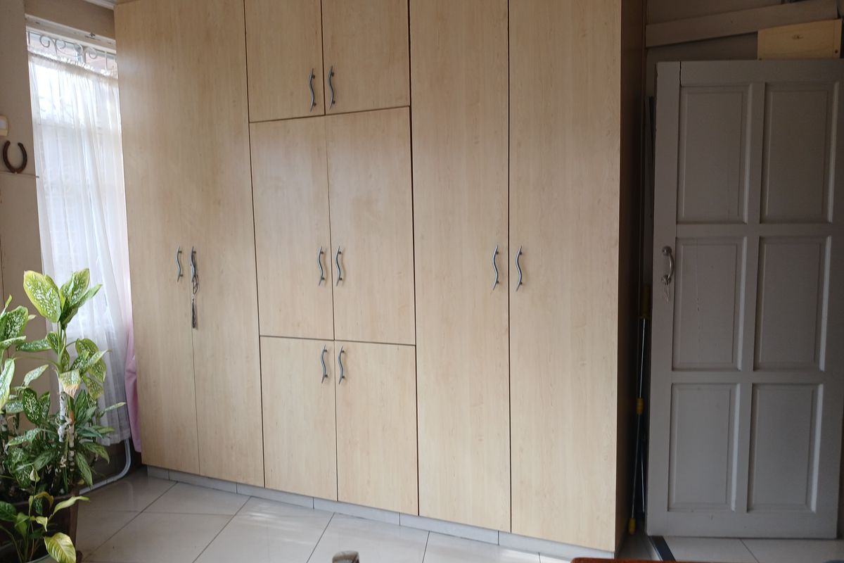 A bedroom featuring floor-to-ceiling light wood built-in cupboards and neutral tiled flooring, providing ample storage space.