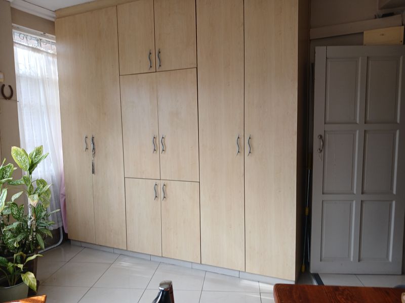 A bedroom featuring floor-to-ceiling light wood built-in cupboards and neutral tiled flooring, providing ample storage space.