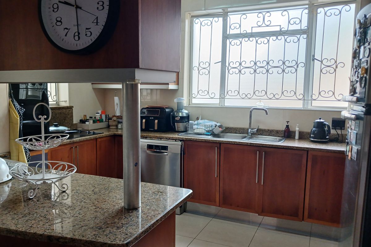 A functional kitchen featuring wooden cabinetry, granite countertops, a stainless steel sink, and tiled flooring, with security bars installed on the window.