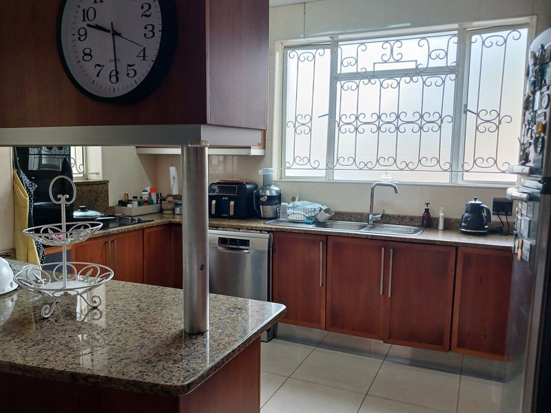 A functional kitchen featuring wooden cabinetry, granite countertops, a stainless steel sink, and tiled flooring, with security bars installed on the window.