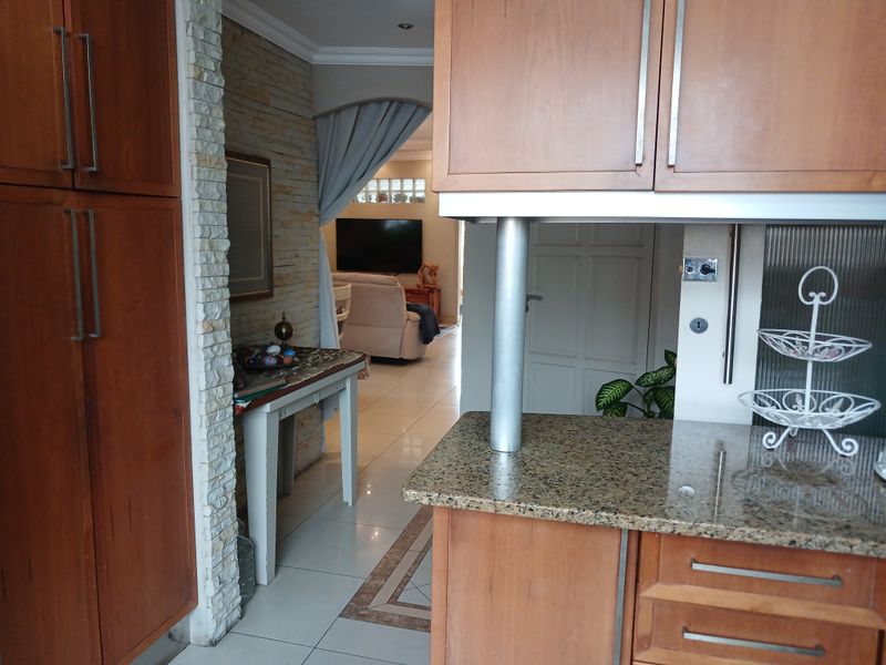 A kitchen area featuring wooden cabinetry, granite countertops, and a stone-clad feature wall, with an open-plan flow leading into the living space.