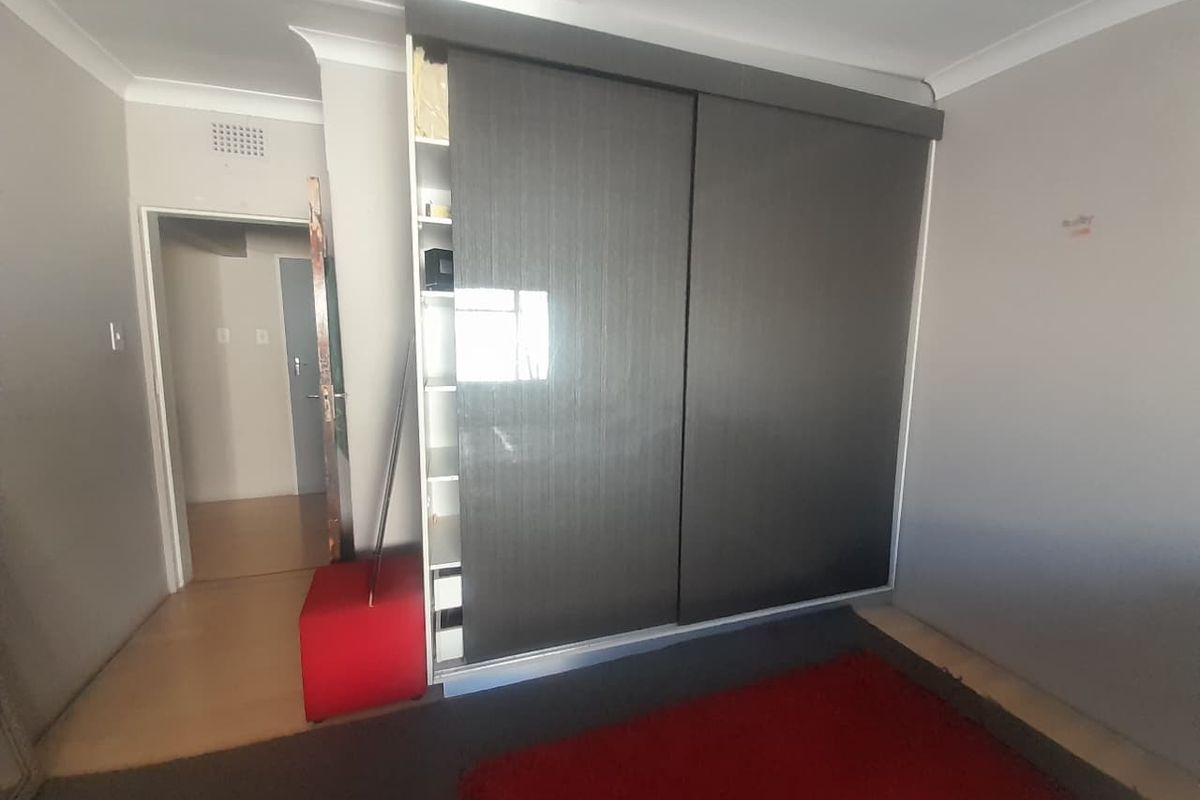A bedroom featuring a modern dark-toned built-in sliding door wardrobe and neutral wall finishes.