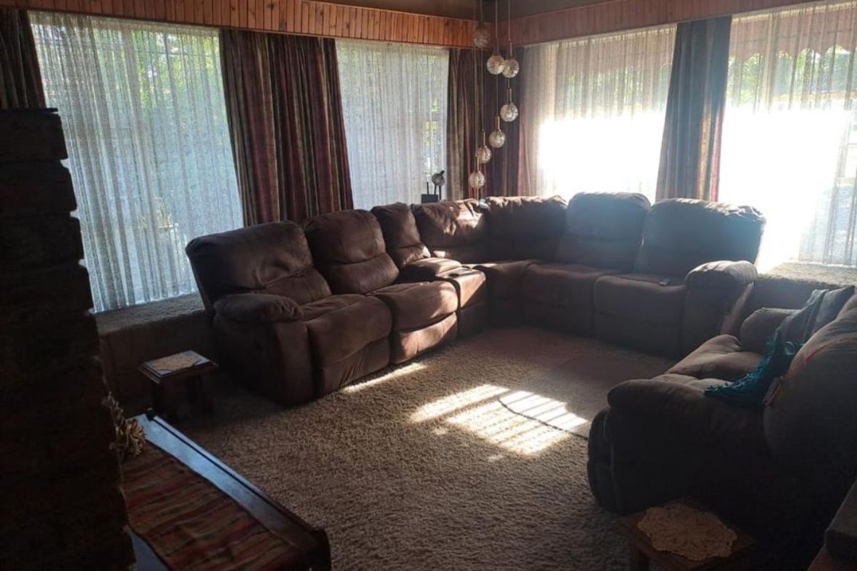 Spacious living room featuring a stone fireplace, timber ceiling paneling, and large windows that provide ample natural light.