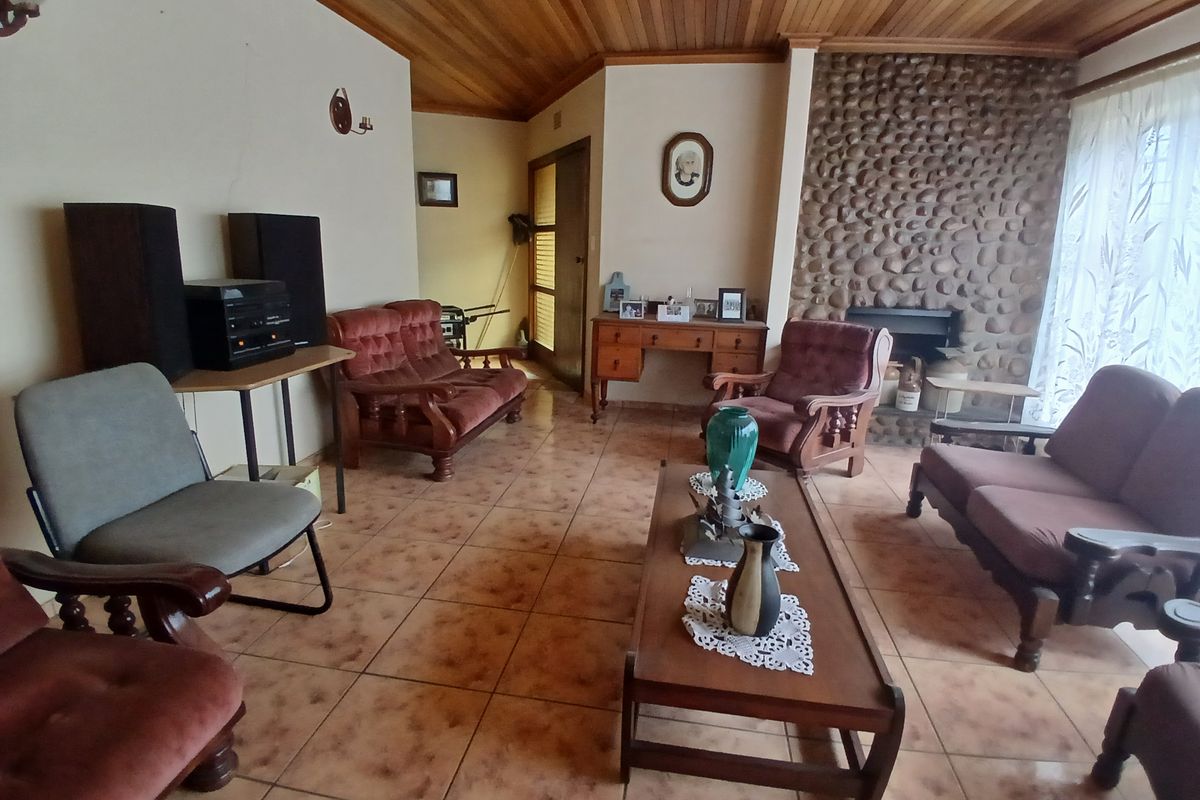 Spacious living room featuring a rustic stone fireplace, timber ceiling, and ceramic tiled flooring, offering a traditional aesthetic with potential for modernization.