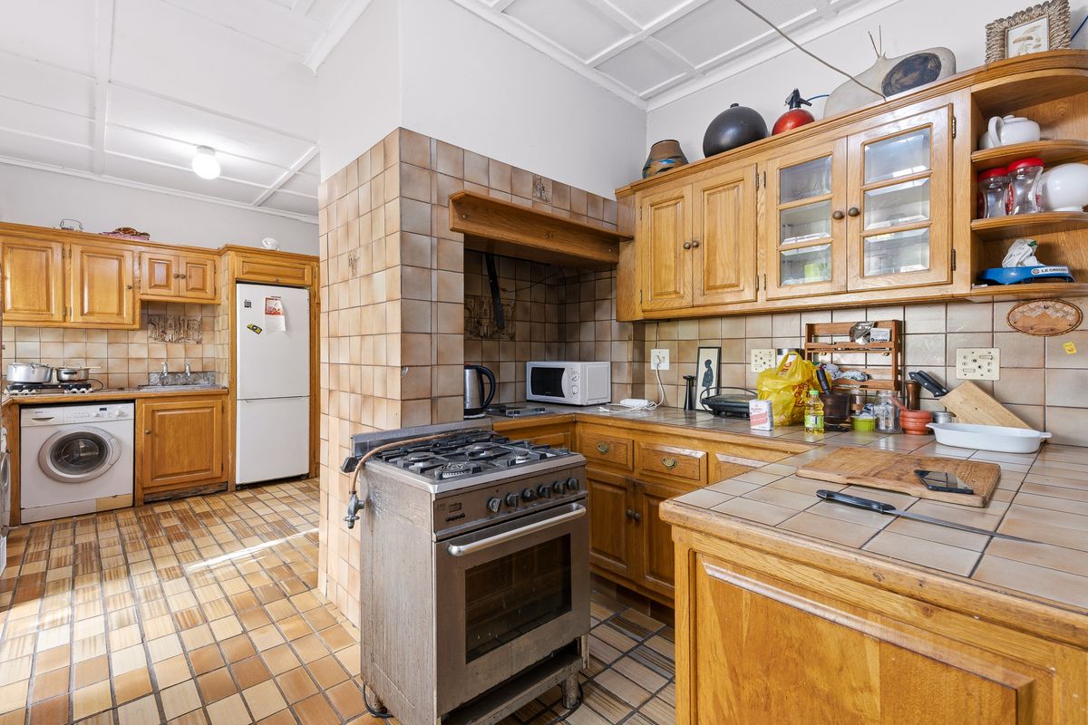 A functional kitchen featuring wooden cabinetry, tiled countertops, a gas stove, and tiled flooring, offering a traditional layout with ample storage space.