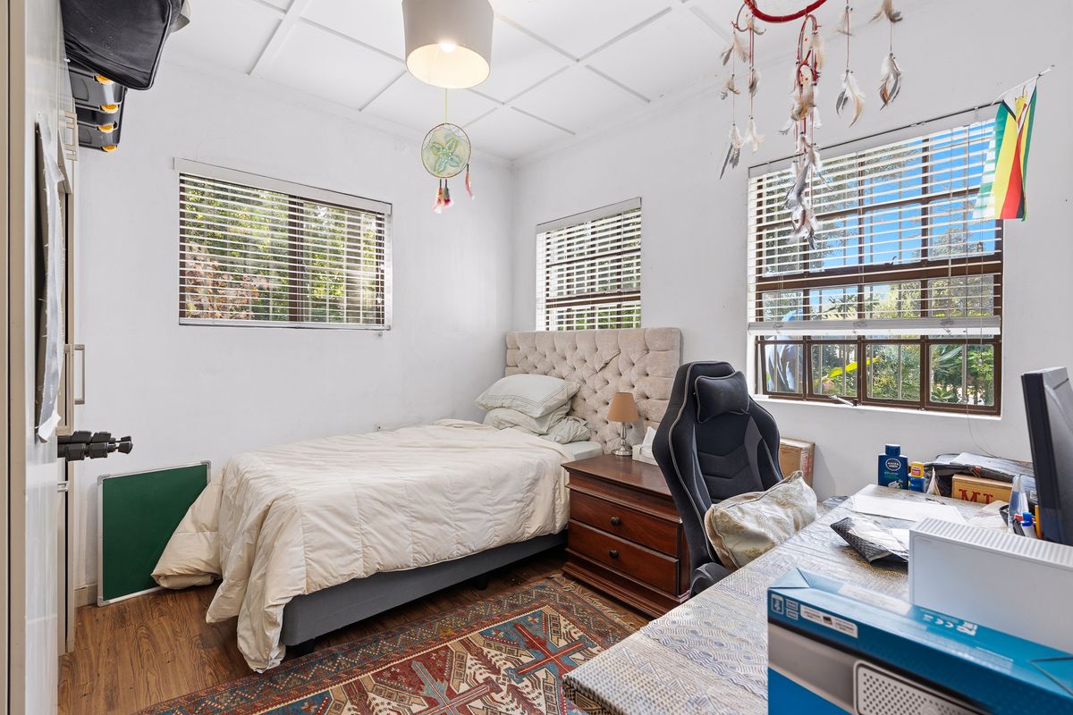 A functional bedroom featuring laminate flooring, a coffered ceiling, and multiple windows with fitted venetian blinds, providing ample natural light.