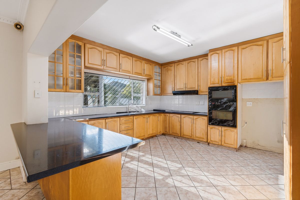 Spacious kitchen featuring wooden cabinetry, dark granite countertops, built-in oven, and tiled flooring with a breakfast bar area.