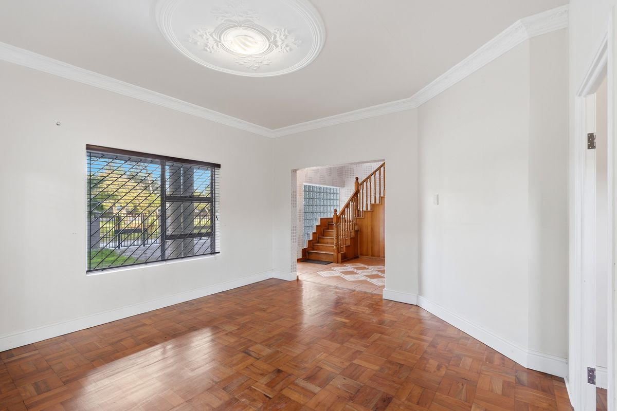 A bright, empty living room featuring classic parquet flooring, decorative ceiling rose, and a view through to the staircase and entrance hall.