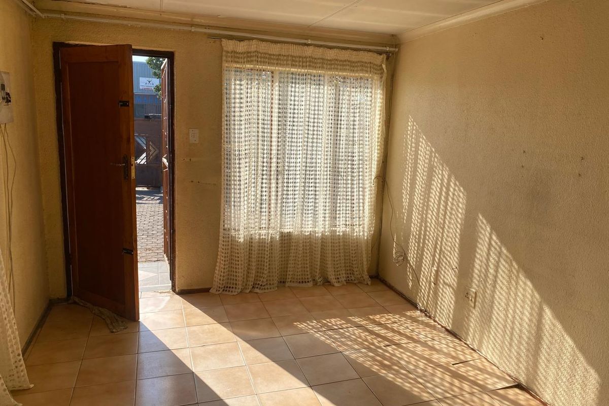 A vacant living room featuring tiled flooring, a single door leading to the exterior, and natural light filtering through window curtains.