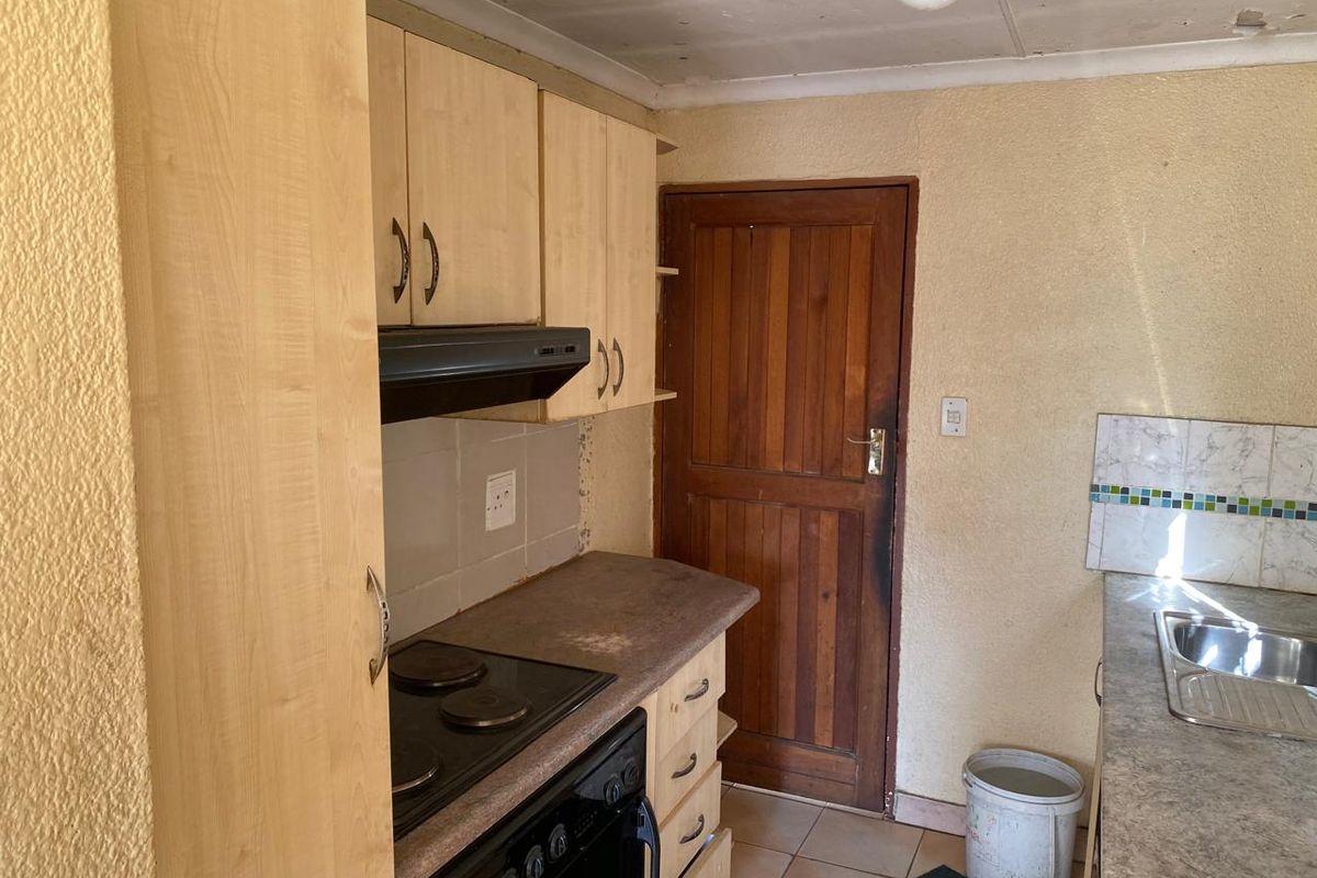 A dated kitchen featuring light wood cabinetry, a built-in electric stove with extractor fan, and a stainless steel sink with tiled backsplash.