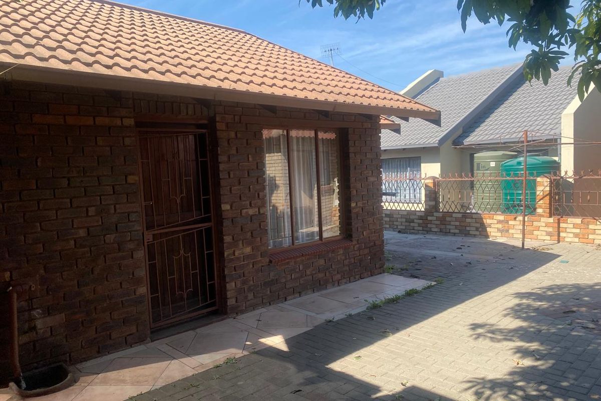 A view of the exterior rear of the house featuring face-brick walls, a tiled roof, and paved outdoor area.