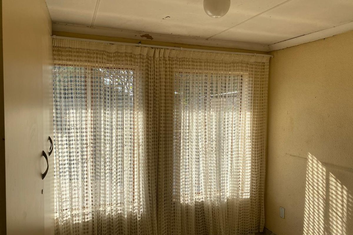 A bedroom featuring dual windows with curtains, showing signs of wear and requiring cosmetic updates to the walls and ceiling.