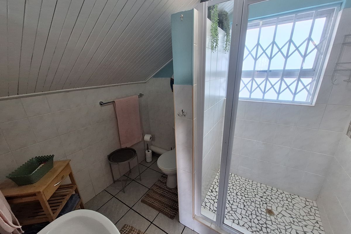 A functional bathroom featuring a walk-in shower with mosaic tile flooring, a toilet, and a sloped timber-paneled ceiling.