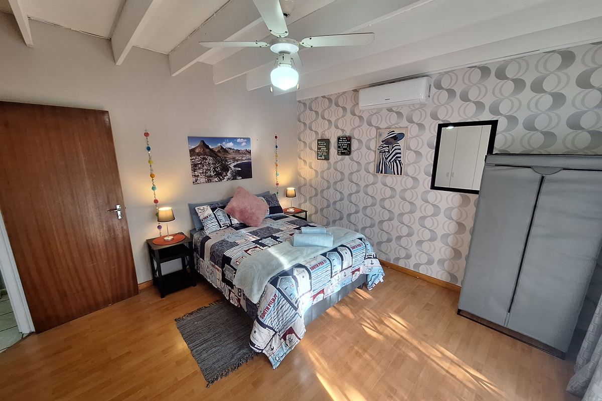 A bedroom featuring laminate flooring, a ceiling fan, and a wall-mounted air conditioning unit.
