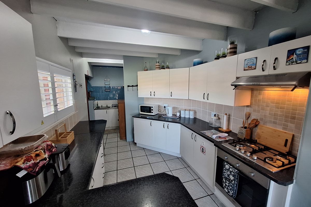 Functional kitchen featuring white cabinetry, dark countertops, built-in gas hob, oven, and extractor fan, with an adjoining scullery area.