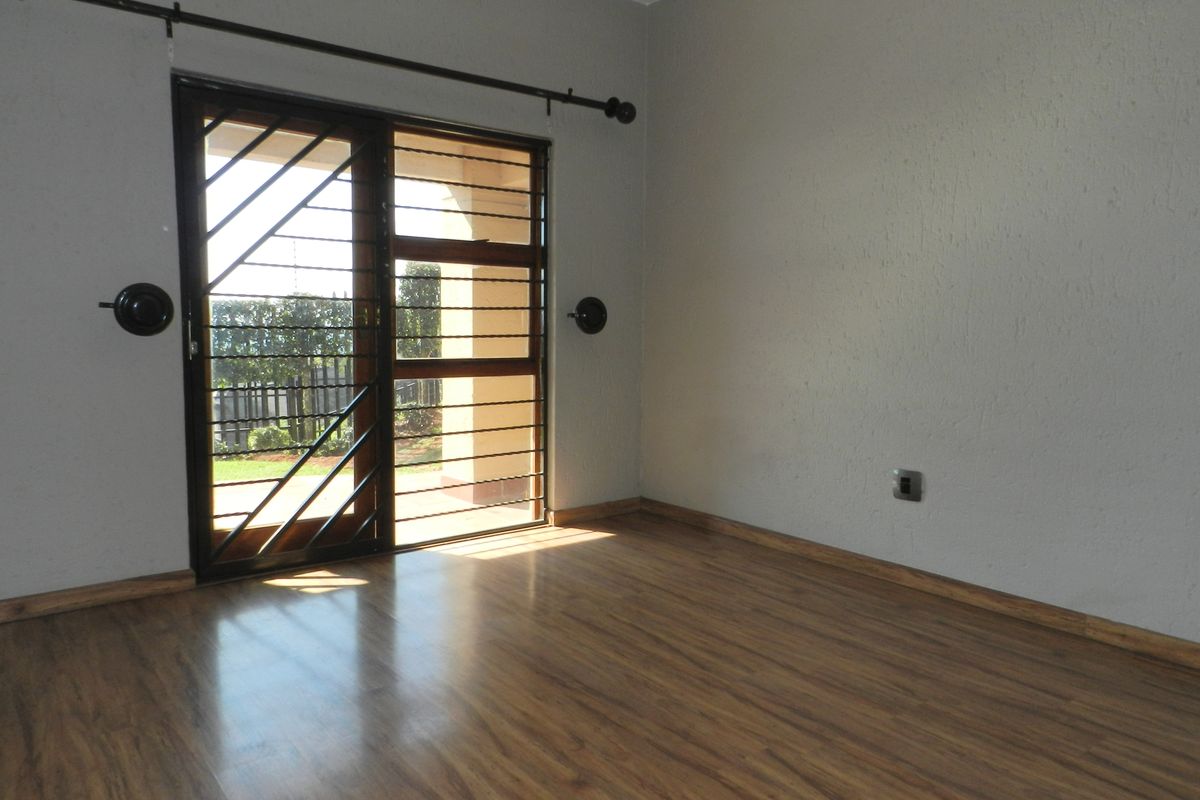 An empty living room featuring laminate flooring and a sliding glass door with an integrated security gate, providing access to the outdoor area.