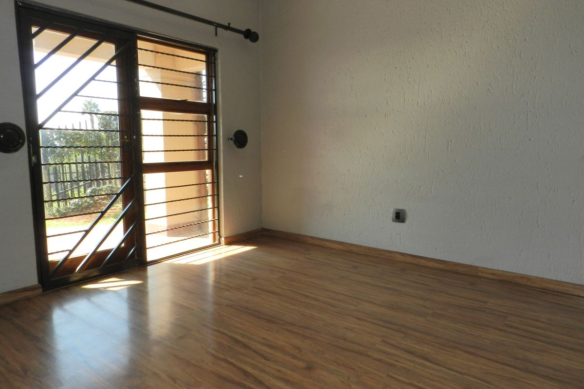 An empty bedroom featuring laminate flooring, textured walls, and a sliding door with an integrated security gate providing access to the exterior.