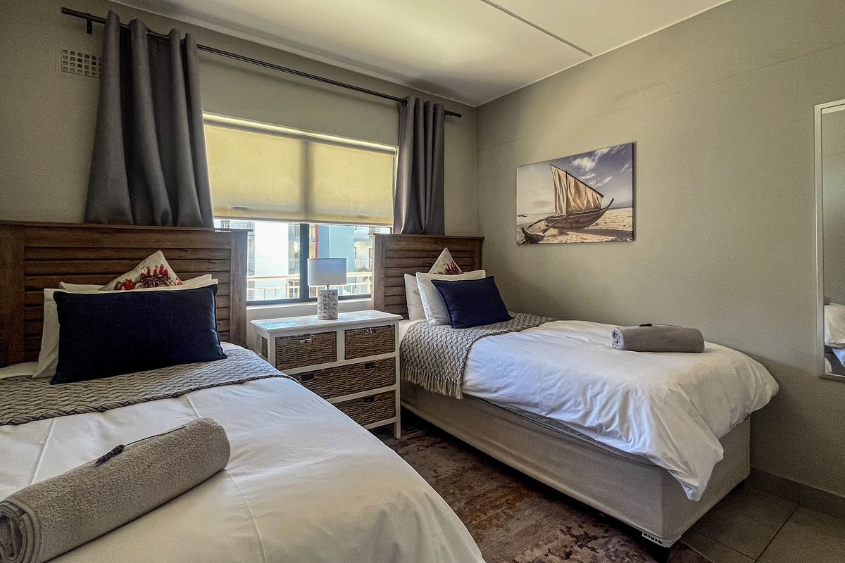 A well-maintained bedroom featuring tiled flooring, neutral wall tones, and a window with roller blinds and curtain tracks.