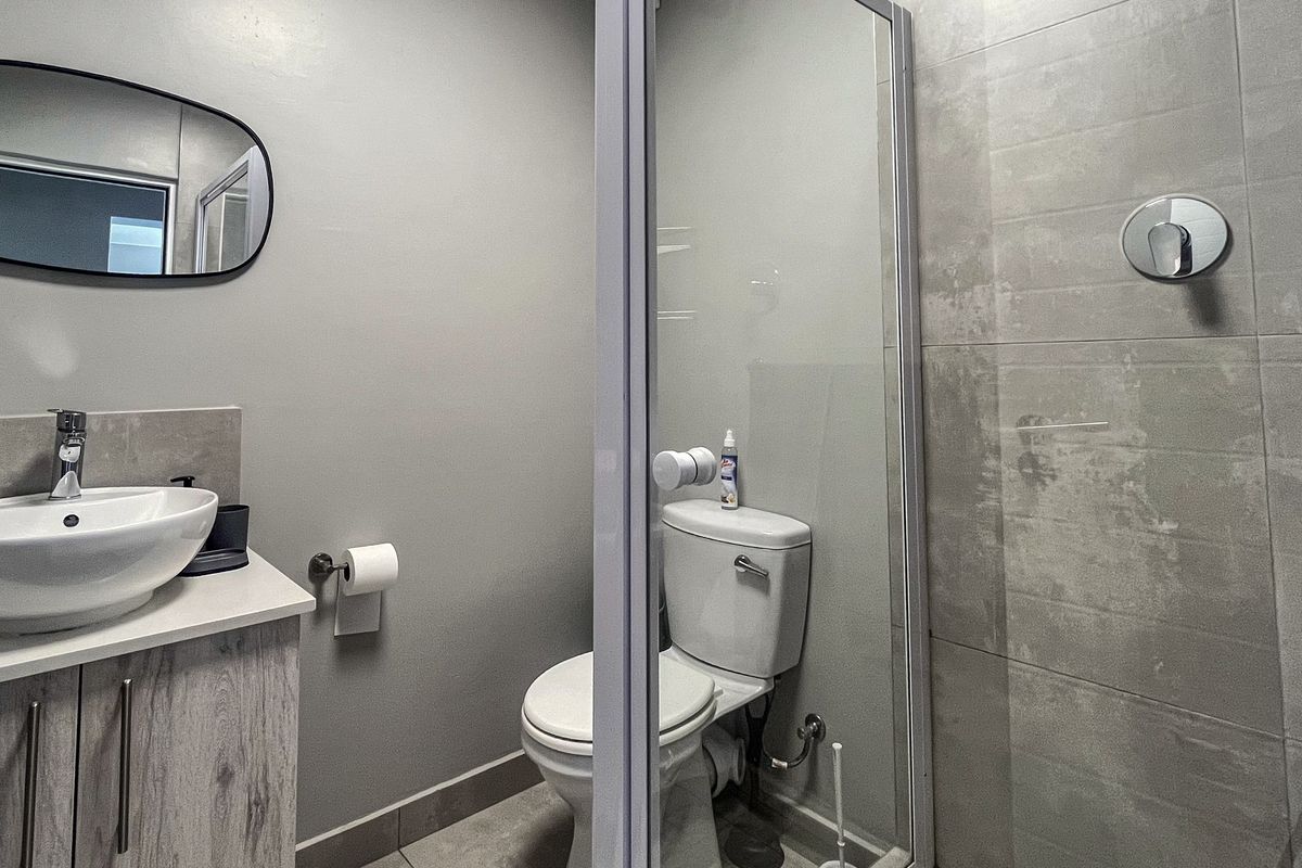 Modern bathroom featuring a vanity with vessel sink, a toilet, and a glass-enclosed shower with grey tiled finishes.