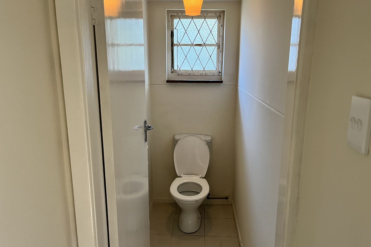 A compact, functional guest toilet featuring tiled flooring and a small leaded glass window for natural light.