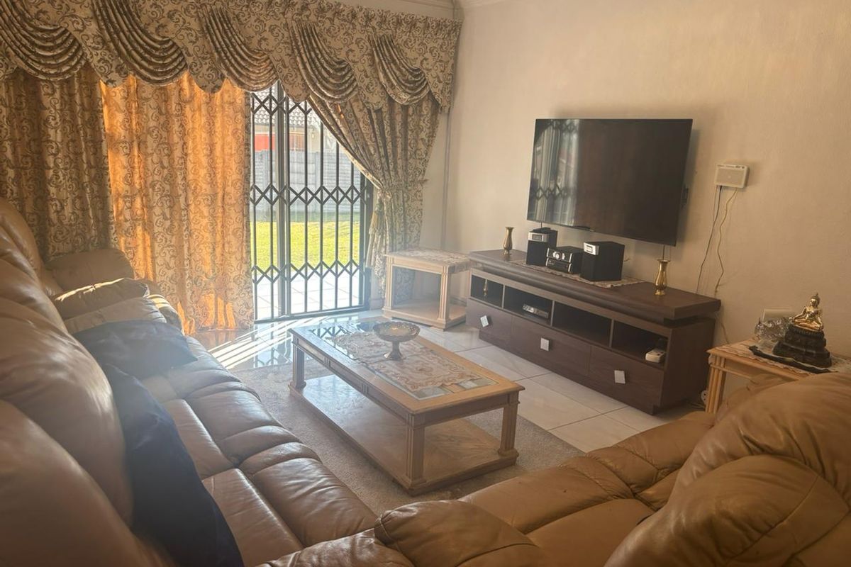 A comfortable living room featuring tiled flooring and a sliding glass door with security gate, providing direct access to the outdoor area.