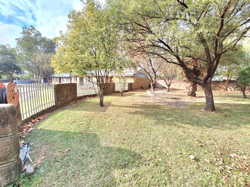 A spacious rear garden featuring established trees, a paved patio area, and perimeter boundary walling with metal fencing.
